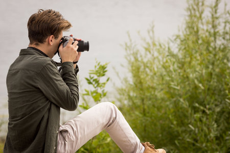 The guy looks into the lens.Young man taking pictures.photography courses.Man holding camera in his hands.Photoshoot.Photographer in nature.Street photography.learning camera settingsの写真素材