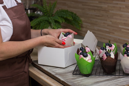 female pastry chef in an apron puts cupcakes in box.Housewife putting dessert in gift box.Food...