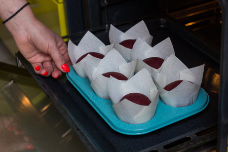 Hands hold the mold with cupcakes and send them to the oven for baking.Pastry chef bakes dessert in the kitchen.Housewife opens the oven and places a baking trayの写真素材