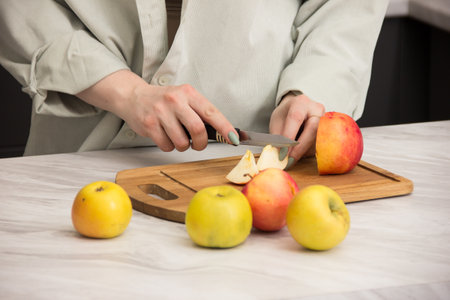 Close-up of woman's hands cutting apples with a knife on a wooden board.Housewife cuts apples into pieces on the kitchen table.Fruits on a cutting board close-upの写真素材