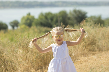Blonde girl in glasses close-up.Baby girl in white dress.Girl with ponytails on her head.Child in...