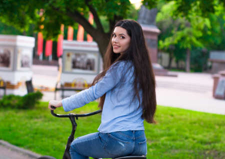 Beautiful young woman with a vintage bicycle in a city parkの写真素材