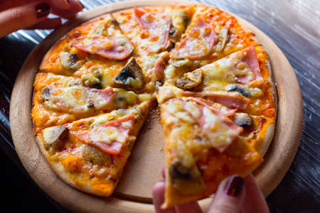 Hot fresh pizza on a wooden plate in female hands. Selective focus.の写真素材