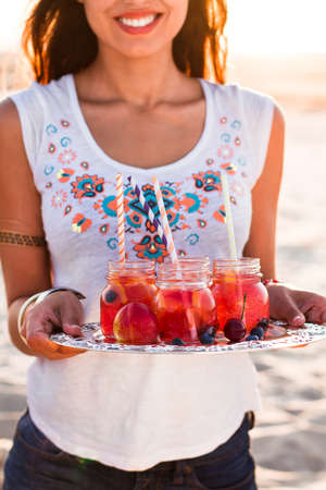 Happy woman holds a dish with a drinks at sunset. Picnic theme