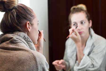 Beautiful young woman apply makeup in the mirrorの写真素材