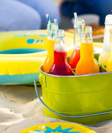 Bottles of lemonade , standing in a colorful green bucket on the beach in the summer sun. Picnic Time!の写真素材