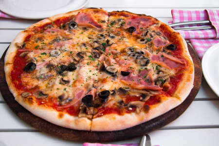 Delicious hot pizza with ham and mushrooms on wooden plate, on white tableの写真素材