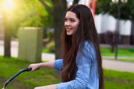 Beautiful young woman with a vintage bicycle in a city parkの写真素材
