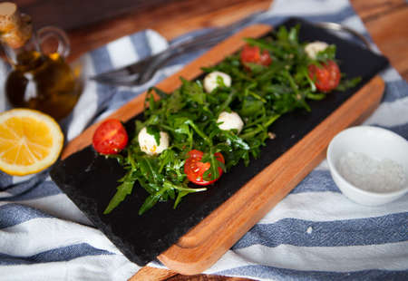 Tasty fresh Italian salad with quail eggs, arugula and tomato with olive oil on wood background in rustic styleの写真素材