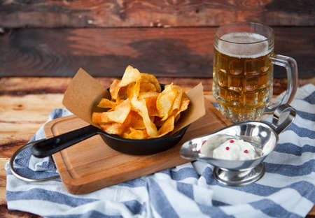 Crackling tasty snack from Homemade potato chips with a glass of cold beer on a dark wooden backgroundの写真素材