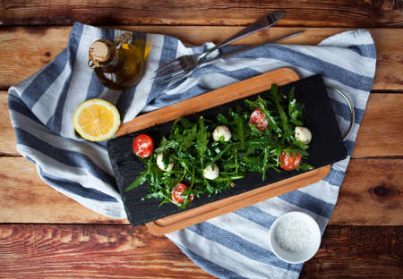 Tasty fresh Italian salad with quail eggs, arugula and tomato with olive oil on wood background in rustic styleの写真素材