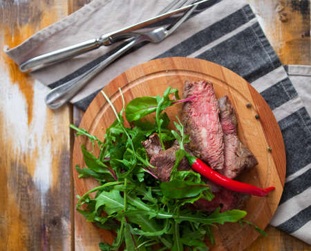 The fragrant cut meat with greens and arugula on a wooden plate against a table in rustic styleの写真素材