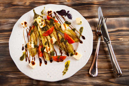 Fried vegetable marrow and tomatoes on white plate with cheese feta and teriyaki sauceの写真素材