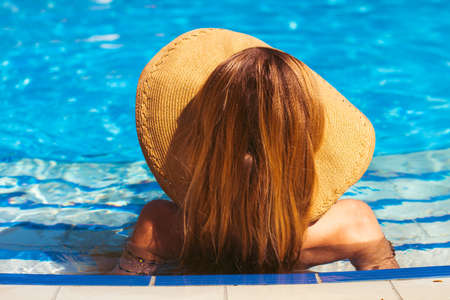 Beautiful blonde woman wearing a hat enjoying the pool, summer time