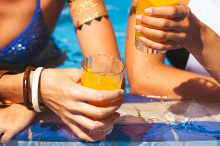 Girlfriends clinking glasses with cocktails at the poolside bar. Summer timeの写真素材