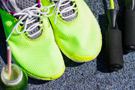 Running shoes, jump rope and drink bottle with green juice on stadium background, Close Up