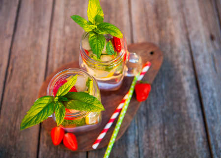 Cold summer drink with mint, strawberry and lemon on an old wooden table in a summer gardenの写真素材