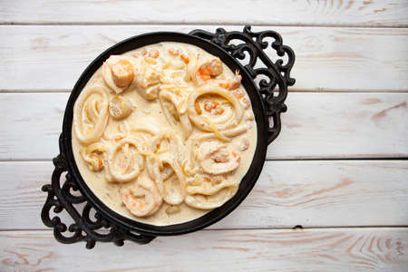 Tasty seafood in white sauce on a metal black plate. Top viewの写真素材
