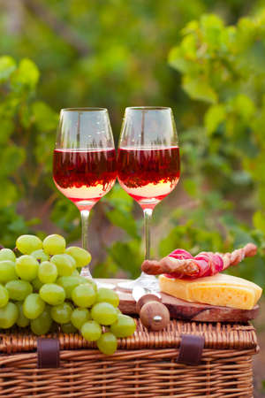 Two glasses of rose wine with meat, grape, bread and cheese on the vineyard backgroundの写真素材