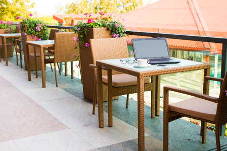 Laptop, glasses, mobile phone and coffee on a wood table in street cafe, business themeの写真素材