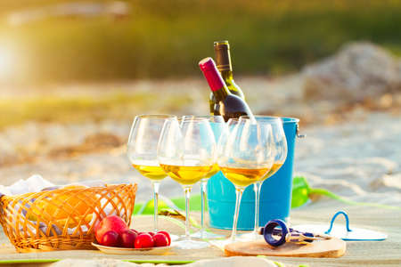 Close Up Glasses of the white wine and fruits on the beach on sunset, picnic theme, summer time.の写真素材