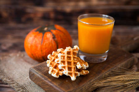 Glass of healhty fresh pumpkin juice with wafer and pumpkin on dark wooden table. Selective focus.の写真素材