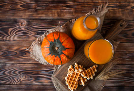 Bottle and Glass of healhty fresh pumpkin juice with wafer and pumpkin on dark wooden table. Top viewの写真素材