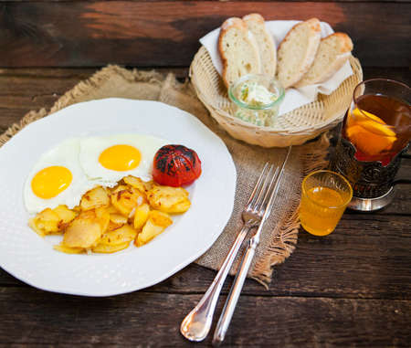 Tea with lemon and plate of breakfast food with eggs, tomato, toast, and fried potatoes, closeupの写真素材