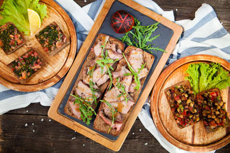 Italian tomato bruschetta with chopped vegetables, herbs and oil on grilled or toasted crusty bread and Cold meat plate and bread on old wood tableの写真素材
