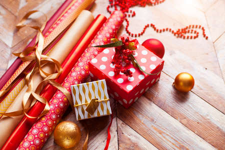 Rolls of Christmas wrapping paper with ribbons, gifts and bolls on wooden backgroundの写真素材