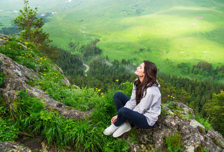 Beautiful woman sitting on mountain top and contemplating landscapeの写真素材