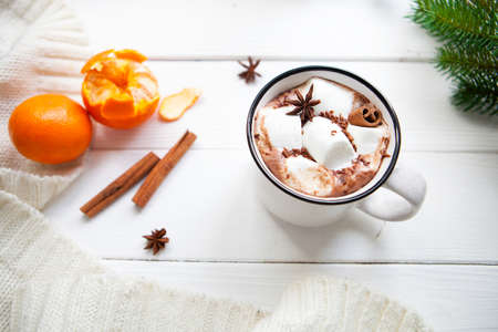 Hot chocolate with marshmallows in a ceramic cup, cinnamon sticks, tangerines and plaid on a white tableの写真素材