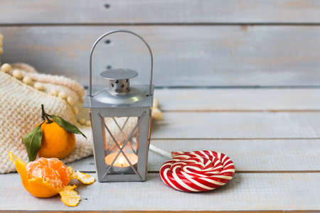 Christmas still life with lantern, plaid, lollipop, tangerine and red beads on grey wooden backgroundの写真素材