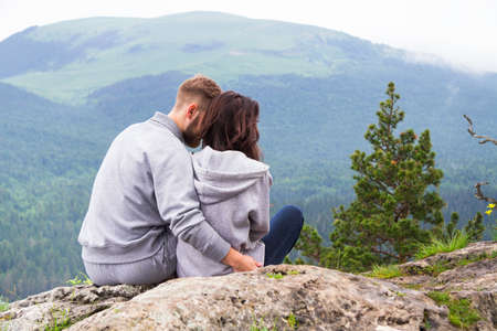 Loving young couple sitting on a mountain, hugging and looking away, love and feelings concept.の写真素材