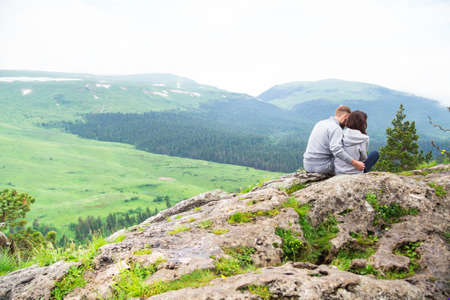 Loving young couple sitting on a mountain, hugging and looking away, love and feelings concept.の写真素材