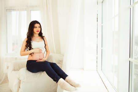 pregnancy, motherhood, people and expectation concept - close up of happy pregnant woman with big belly at windowの写真素材