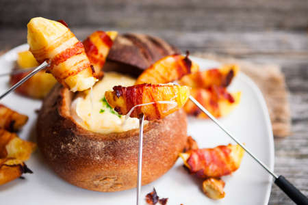 Tasty hot cheese fondue served in a bread roll with potatoes and bacon, close upの写真素材