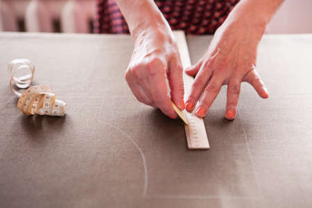 Close up. hands woman Tailor working cutting a roll of fabric on which she has marked out the pattern of the garment she is making with tailors chalk.の写真素材
