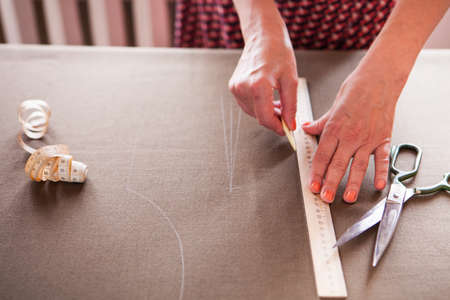 Close up. hands woman Tailor working cutting a roll of fabric on which she has marked out the...