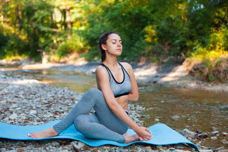 Young beautiful woman meditating near the mountain river. Yoga practicing outdoors.の写真素材