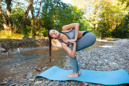 Young beautiful woman meditating near the mountain river. Yoga practicing outdoors.の写真素材