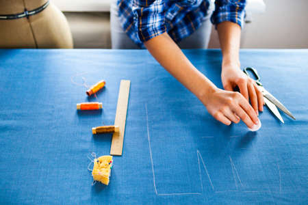 Close up. hands woman Tailor working cutting a roll of fabric on which she has marked out the pattern of the garment she is making with tailors chalk.の写真素材