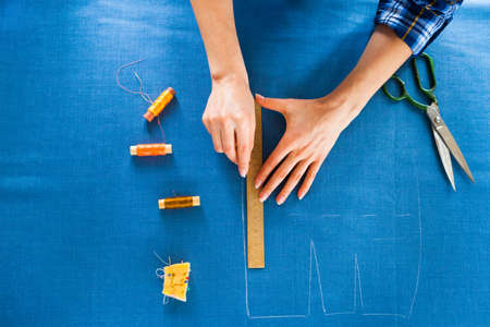 Close up. hands woman Tailor working cutting a roll of fabric on which she has marked out the pattern of the garment she is making with tailors chalk.の写真素材