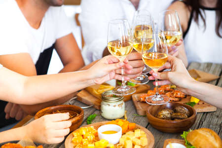 Hands with white wine toasting over served table with food. Friends Happiness Enjoying Dinning Eating Concept.の写真素材