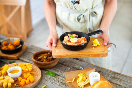 Long-haired beautiful woman in apron holds a tray with food in her hands. Waiter serves food. Food and drink conceptの写真素材