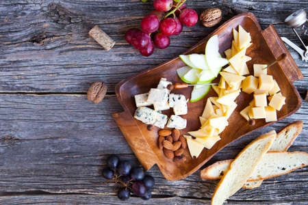 Wine snack set. Glass of red and white wine, grape, cheese, over rustic wooden background. Top view, copy space, horizontal composition.の写真素材