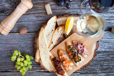 Wine snack set. Glass of red and white wine, grape, cheese, over rustic wooden background. Top view, copy space, horizontal composition.の写真素材