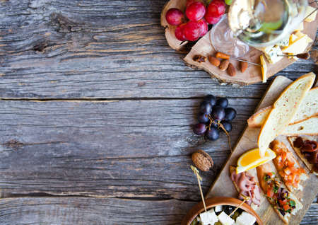 Wine snack set. Glass of white wine, grape, cheese, over rustic wooden background. Top view, copy space, horizontal composition.の写真素材