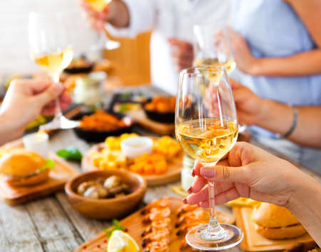 Hands with white wine toasting over served table with food. Friends Happiness Enjoying Dinning Eating Concept.の写真素材