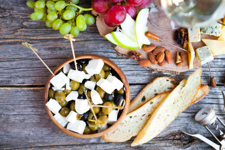 Wine snack set. Glass of white wine, grape, cheese, over rustic wooden background. Top view, copy space, horizontal composition.の写真素材